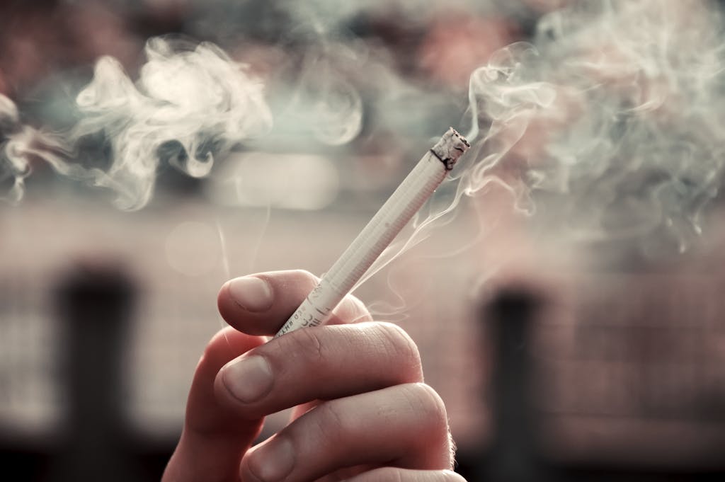 A close-up view of a hand holding a lit cigarette, with smoke visible in the air.