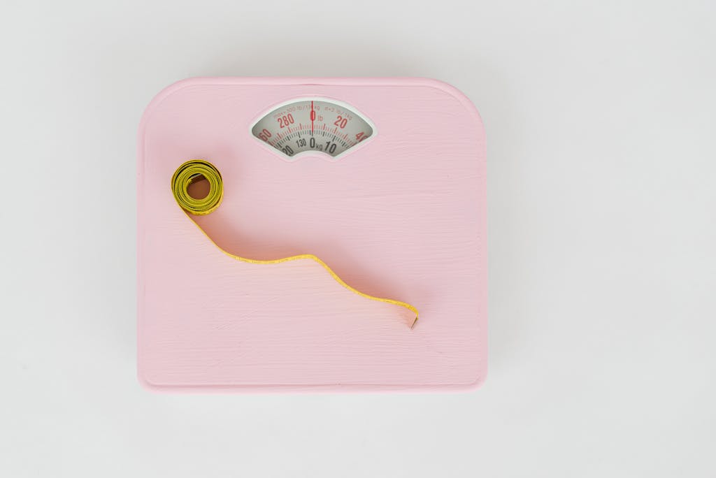 A pink weighing scale paired with a yellow measuring tape on a white backdrop.