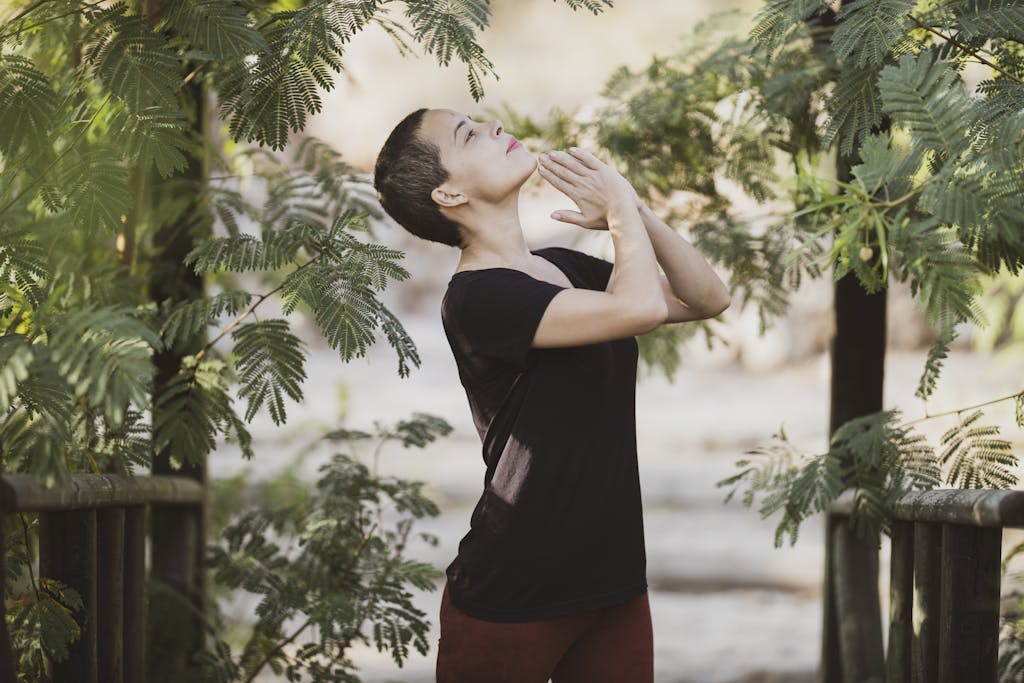 A woman practices meditation surrounded by lush green foliage, enjoying a peaceful moment outdoors.